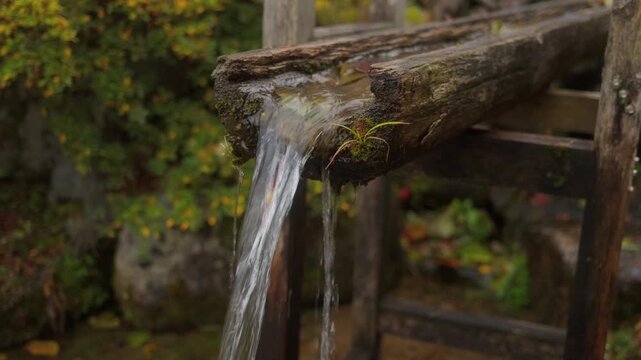 Fresh clear water flowing from rustic wooden fountain in Japan. Close up detail of traditional water feature with natural texture and peaceful atmosphere.