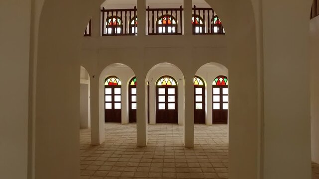  Bright interior courtyard hall with rows of arches and colored windows, revealing symmetrical architecture and spacious design of a preserved historic cultural building. 