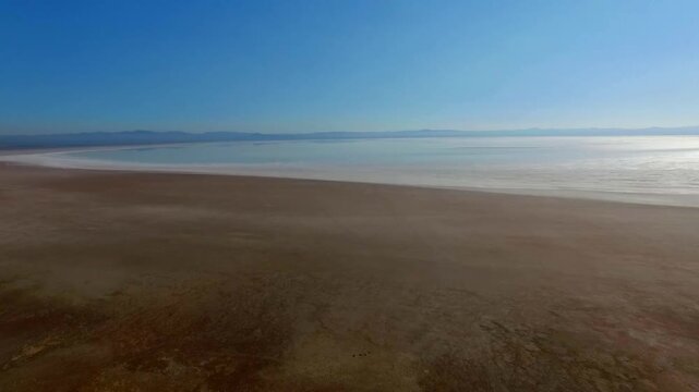  Aerial view of wide salt lake shoreline with smooth gradient from shallow to deeper water, highlighting abstract patterns, earthy tones and minimal landscape composition. 
