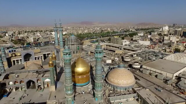  Aerial view of a golden dome shrine and turquoise minarets rising above a dense urban district, capturing sacred Islamic architecture, pilgrimage atmosphere, and the surrounding cityscape. 