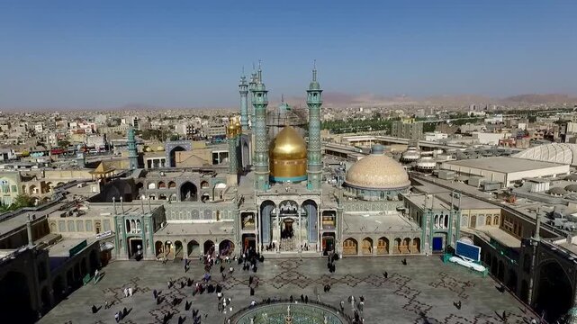  Frontal aerial perspective of a revered shrine with gleaming golden domes and blue minarets, emphasizing symmetry, sacred architecture, urban density, and the spiritual heart of the city beyond. 