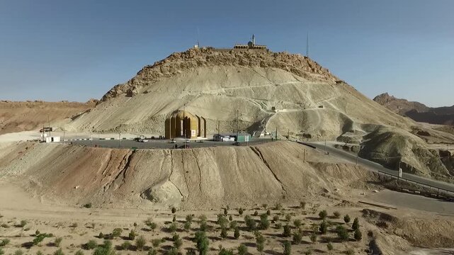  Wide aerial view of a conical desert hill with a shrine entrance carved into its base, capturing dramatic geology, religious significance, and the stark contrast between faith and terrain. 