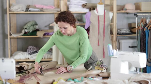 Woman tailor cuts paper dress pattern and work with hand snip. Process of manual production of clothes. Individual production of fashionable clothes, unique handmade products 