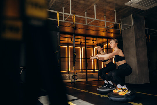 Women doing squats on bosu balls in gym