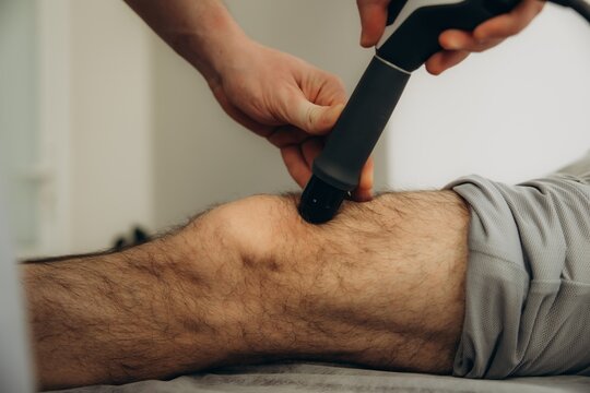 Physiotherapist using shockwave therapy on person's knee