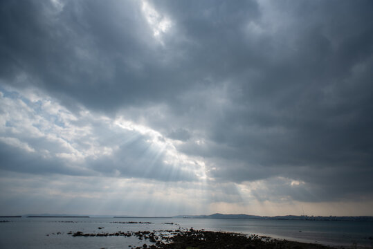 曇天の雲の隙間から日差しが差す海上