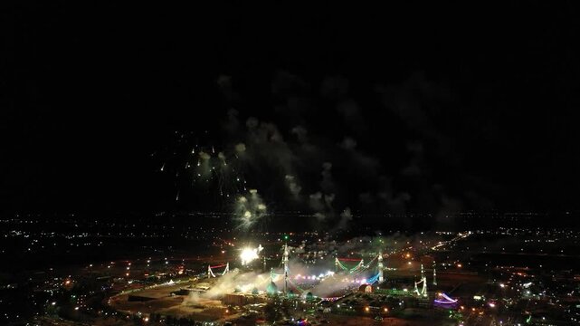  Aerial view captures stunning fireworks exploding above a mosque and cityscape, showcasing a vibrant celebration, urban environment, and the presence of a significant spiritual landmark. 