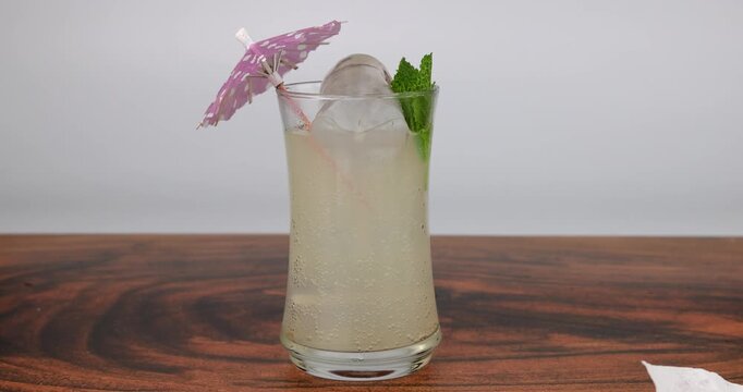 Summer lemonade drink with ice and mint sprig on mahogany wood table while placing a pink cocktail umbrella on white background.