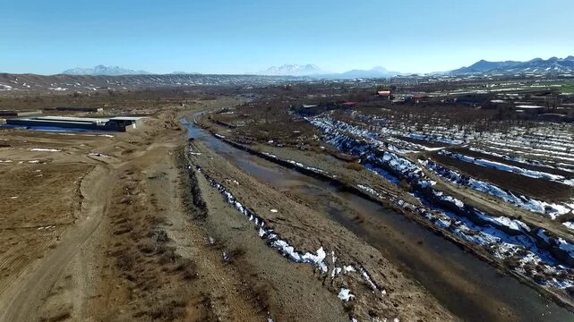  Wide aerial view of a river cutting through a dry desert landscape with patches of snow along the banks. Shows the cold, harsh environment and the contrast of water in an arid land region. 