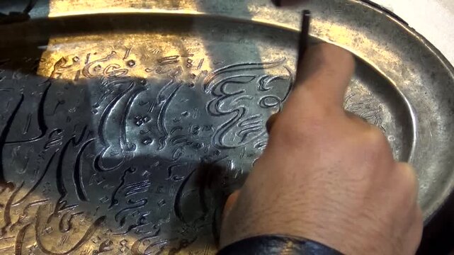  Close up of metal engraving showing a hand carving intricate Persian inscriptions on silverware, illustrating traditional craftsmanship, culture, and skillful artistry. 