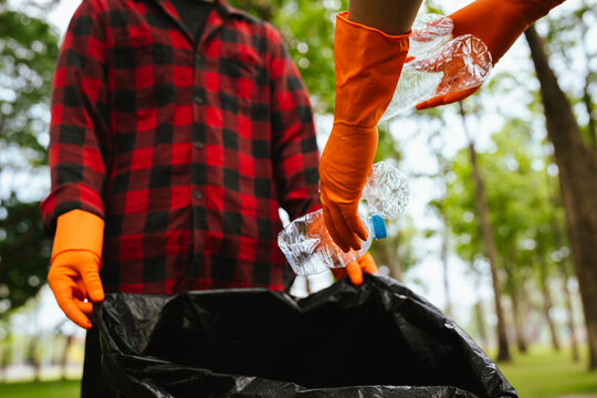 Person wearing gloves placing a plastic bottle into a trash bag in a park, highlighting recycling, environmental cleanup, and responsible waste management outdoors.