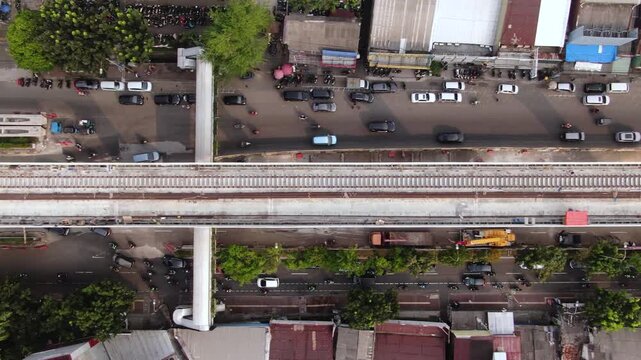 Aerial top down view of elevated railway track and pedestrian bridge over busy city road. Metropolitan infrastructure development featuring public transport project and urban traffic flow