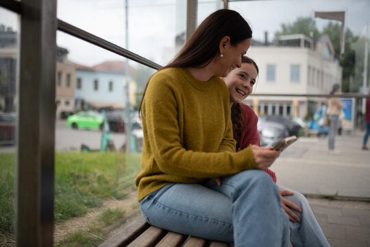 Woman and teenage girl waiting at bus stop.