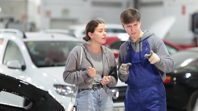 Male mechanic advises young woman client on repairing of car in car service station. High quality 4k footage