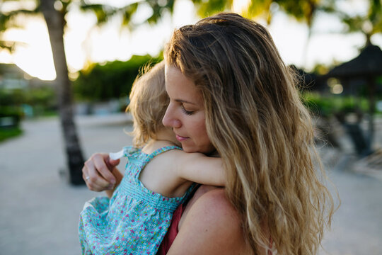 Mother embracing her little daughter in tropical beach resort.
