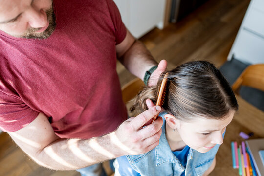 Dad brushing daughter hair and making braid at home.