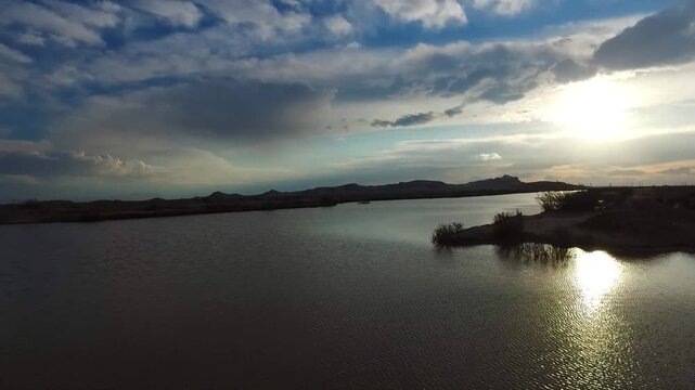  Calm salt lake water reflecting dramatic clouds and distant hills under soft evening light. A peaceful desert basin scene with still surface and natural horizon creating a tranquil atmospheric