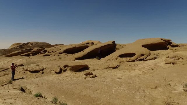  Low sandstone slabs spread across a sandy desert floor, showing smooth weathered surfaces, natural rock patterns, and the quiet openness of an arid geological landscape today. 