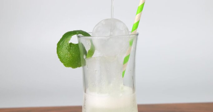 Rotating glass of fresh lemonade with ice cubes and green mint leaves featuring a sustainable paper straw on white background.