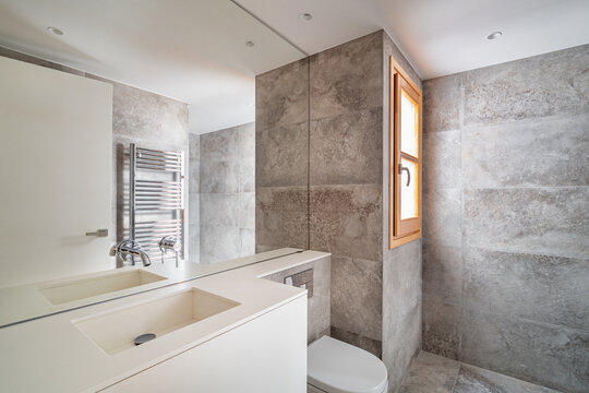 Modern bathroom with gray stone walls, white sink, and wooden window. Clean and minimalist design, featuring a towel radiator and natural light.