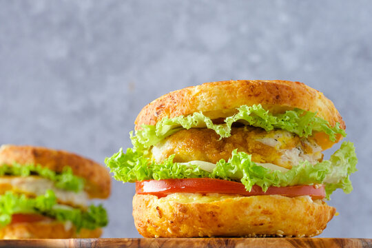 Two bagel sandwiches on a cutting board, filled with crispy chicken, lettuce, and tomato on a gray background. Modern breakfast concept and healthy morning routine.