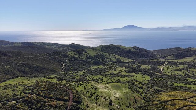 Drone pans across vibrant green valleys and rugged peaks in Tarifa, revealing the distant blue waters of the Mediterranean and African mountains.