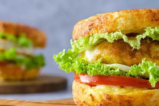 Close up bagel sandwiches on a cutting board, filled with crispy chicken, lettuce, and tomato on a gray background. Modern breakfast concept and healthy morning routine.