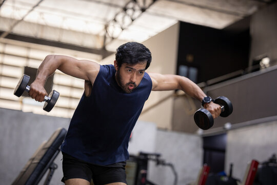 Fitness gym dumbbell workout exercise strength training muscular man weightlifting training session, focused athletic man performing bent over dumbbell fly exercise for shoulder workout inside