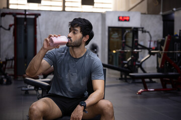 Naklejka premium Fitness gym athlete man drinking protein shake muscular workout hydration recovery, male athlete drinking protein shake after workout gym, sweaty muscular fitness man resting bench for hydration