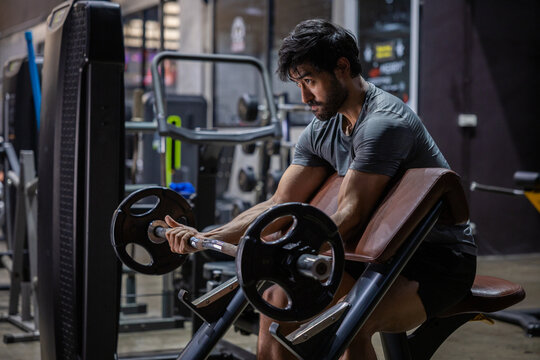 Barbell bicep curl gym fitness strength training Young athletic man doing barbell bicep curl preacher bench modern gym, focused expression, muscular arm workout with weight plate equipment