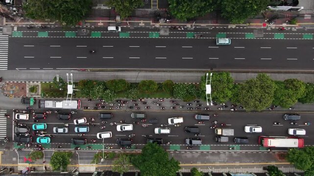 Aerial top down view of heavy traffic congestion on a city main road. High angle shot featuring crowded motorcycles, public bus, and green bicycle lanes in the heart of Southeast Asia's busiest