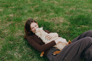 Fototapeta premium Lifestyle moment of a woman outdoors, lying on grass and cuddling a goat kid, gentle smile, soft breeze, warm tones, natural setting, relaxed mood, affectionate connection with nature.