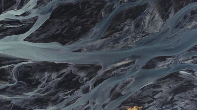 Drone view of braided rivers in Iceland, showing winding water channels across a glacial plain. Abstract natural patterns in a dramatic Arctic landscape.