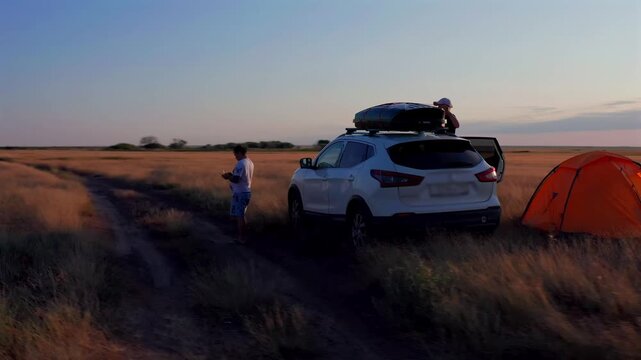 Man standing near car and camping tent in open steppe at sunset in Kostanay region Kazakhstan, road trip travel lifestyle, outdoor adventure, freedom, exploration in vast natural landscape