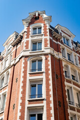 Obraz premium Low angle view of a traditional red brick residential building in Lille, France. The facade features white stone trim around windows and decorative gables under a blue sky.