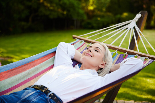 Mature woman resting in colorful hammock in backyard garden
