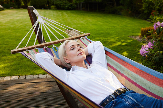 Mature woman resting in colorful hammock in backyard garden