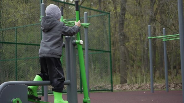 Little boy exercising on an elliptical trainer machine at an outdoor gym, promoting a healthy and active lifestyle for children with regular cardio fitness and physical training