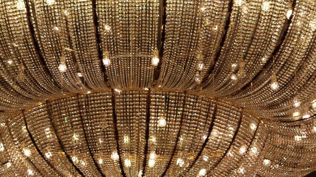 Golden chandelier hangs above elegant room. Crystal strands glow warmly from many lights. Each facet catches light with brilliance. Luxury radiates from ceiling fixture
