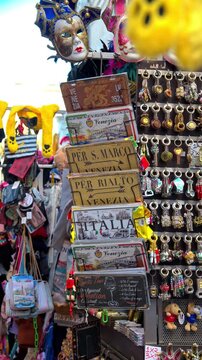 Souvenir stall selling colorful Venetian masks and decorative metal signs in a historic Italian city.