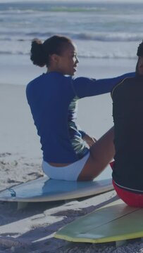 Vertical video: Woman on white surfboard listening to companion and pointing toward ocean for surf