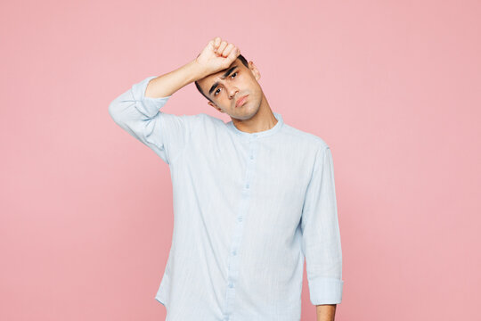 Young sad sick ill exhausted dissatisfied middle eastern man wear casual blue cotton shirt put hand on forehead isolated on plain pastel light pink wall background studio portrait. Lifestyle concept.