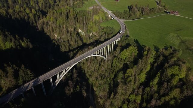 Drone side tracking shot of a bus traveling across a large bridge over a deep valley, showing public transport and infrastructure.