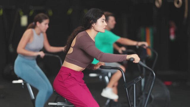 Latina woman doing circuit cardio workout on air bike in Crossfit gym. Athletes develop muscular endurance. High quality 4k footage