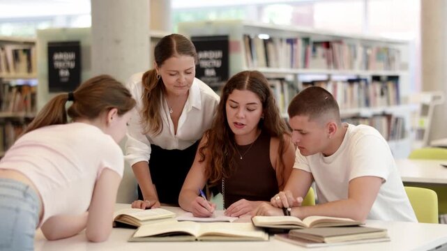 Group of student sits at table in library and studies, reads books and takes notes, makes summary, deliberative meeting, collective work. Preparation for exams, educational process, additional classes