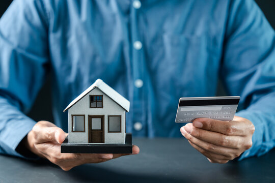 Real estate and mortgage concept. Person holding model house and credit card.