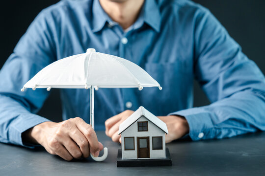 Person holding umbrella over model house. Real estate and property insurance concept.