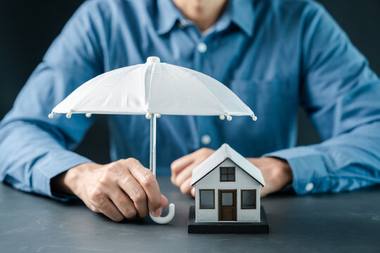 Real estate and property insurance concept. Person holding umbrella over model house.