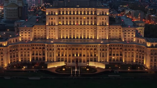 Aerial drone footage showing palace of parliament illuminated at night, bucharest city center building in motion.