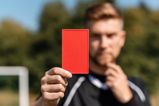 Focused soccer referee stands on field, holding up red card to signal penalty or expulsion during competitive game. High quality photo
